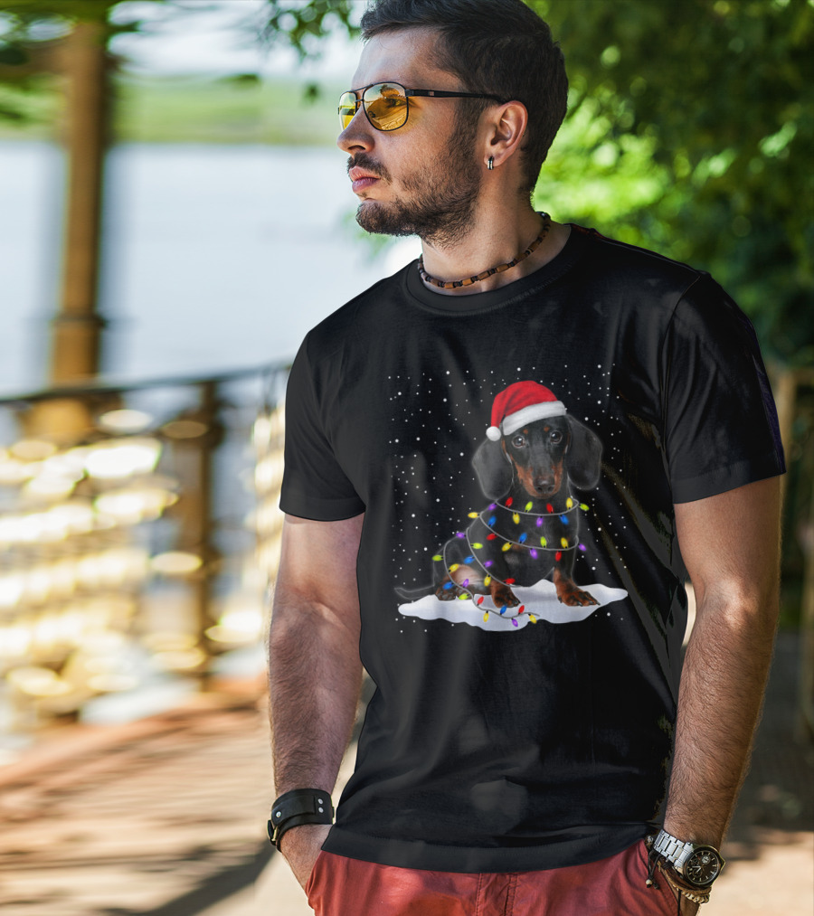 Dachshund Santa Hat Wrapped In Christmas Tree Lights In Snow With Falling Snowflakes T-Shirt